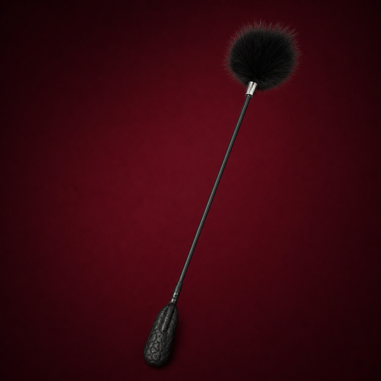 Black crinkle leather feather tickler with a fluffy round head on a deep burgundy studio background.