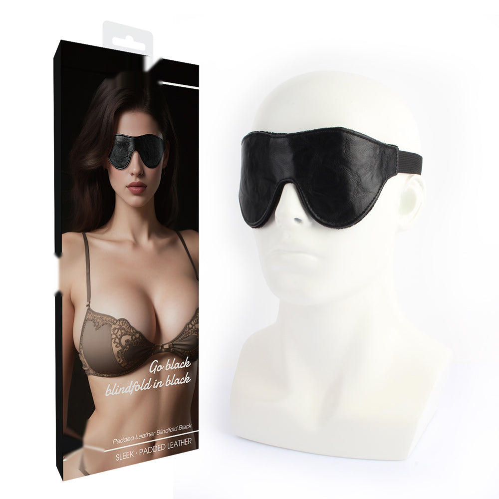 Black padded leather sleep mask shown on a white mannequin head next to its retail packaging box, which features a model wearing the mask.