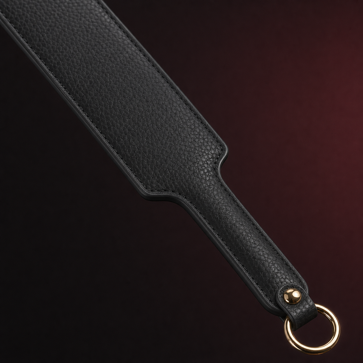 Close-up of the black pebbled leather paddle, stitched edge, gold-tone fastener, and hanging ring.