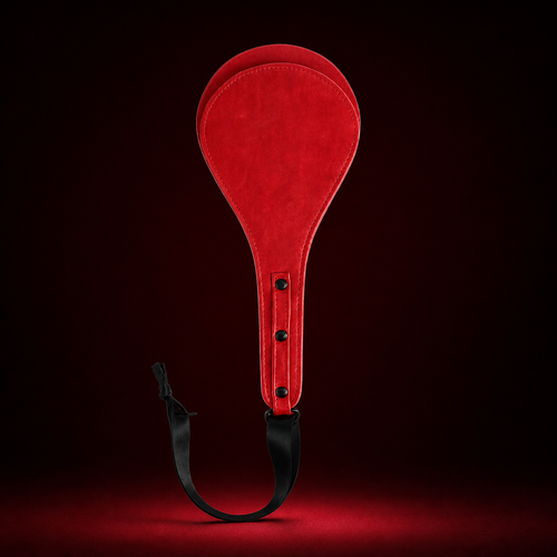 Red round leather paddle with three black rivets and a black wrist strap on a deep burgundy background.