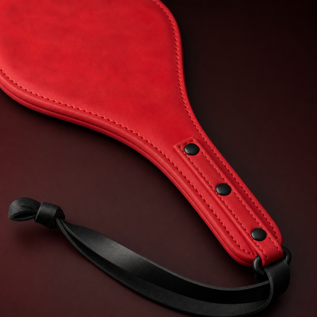 Close-up of the red leather paddle stitching, three black rivets, and black wrist strap.
